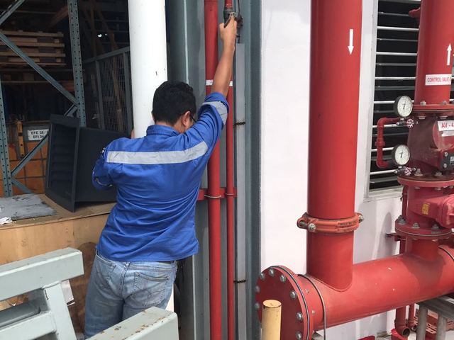 Technician inspecting red fire pipework and a valve